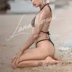 Premium escort model leaning against beach rock in minimalist micro bikini – Phuket