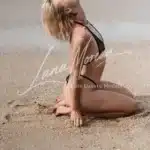 Phuket elite escort girl lying in black bikini on beach, waves in the background